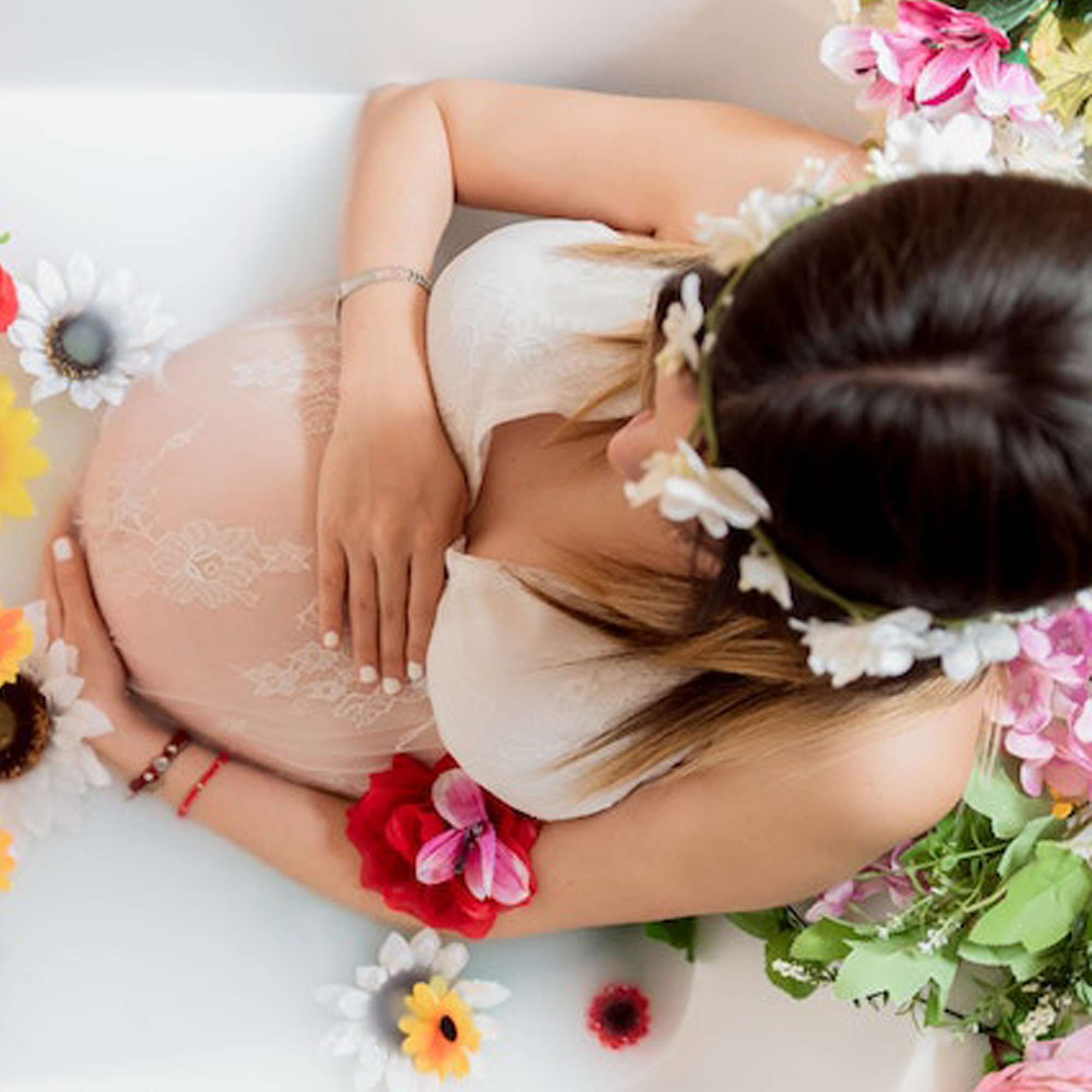 A pregnant woman lying in a milk bath with flowers portraying skincare during pregnancy.